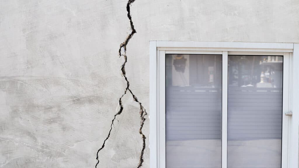 A cracked wall near a window shows infrastructure damage, highlighting climate change and natural disasters' impact.